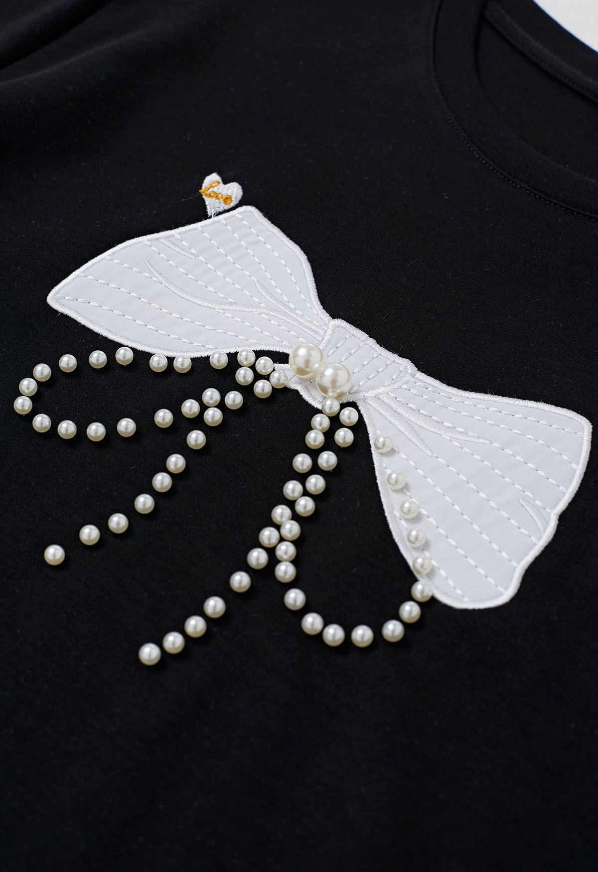 Camiseta negra con adornos de perlas y estampado de lazo