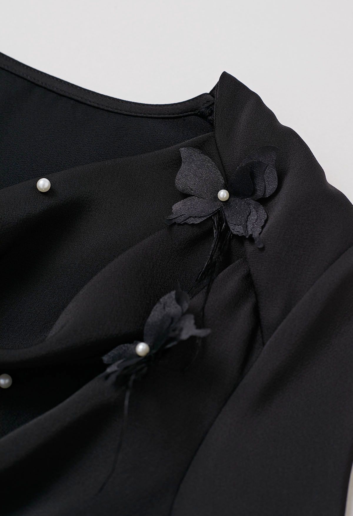 Blusa con cuello vuelto y ribete de plumas de mariposa perladas en color negro